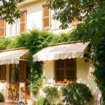 Maison lumineuse aux volets fermés, protégée du soleil par un store extérieur et une végétation abondante qui ombrage la façade en été.