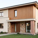 Maison individuelle en rénovation soignée, avec une façade associant crépi, brique, pierre naturelle et bardage bois, éclairée par une lumière naturelle douce.